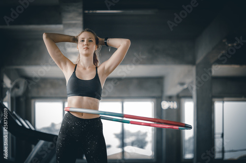 Beautiful caucasian young woman doing hula hoop in step waist hooping forward stance. Young woman doing hula hoop during an exercise class in a gym. Healthy sports lifestyle  Fitness  Healthy concept.