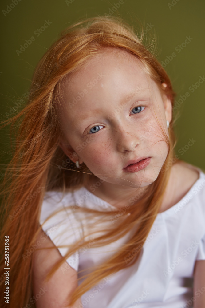 Young red-haired girl with long beautiful hair and big blue eyes. Hair the color of fire fluttering in the wind. Girl child with a brooding mysterious gaze portrait Young red-haired girl with long beautiful hair and big blue eyes. Hair the color of fire fluttering in the wind. Girl child with a brooding mysterious gaze portrait