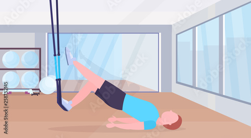 sporty man doing exercises with suspension fitness straps elastic rope guy training crossfit workout concept modern gym studio interior horizontal flat full length