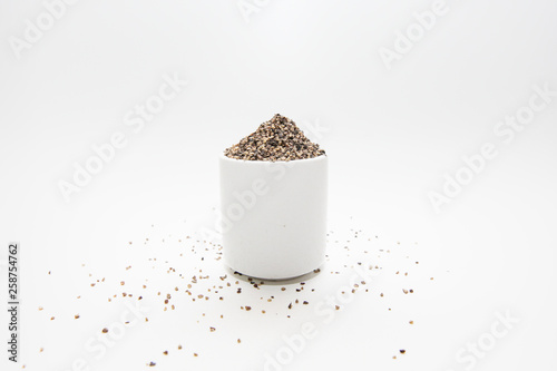Finely ground black pepper in white ceramic bowl isolated on white.