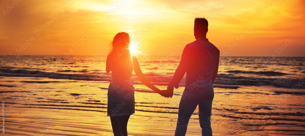 Young couple looking at the romantic, tropical sunset - obrazy, fototapety, plakaty 