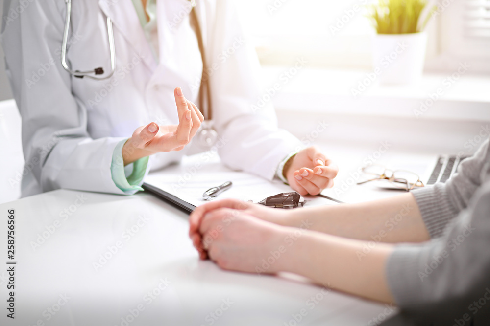 Doctor and  female patient sitting at the desk and talking  in clinic near window. Medicine and health care concept. Green is main color