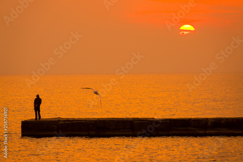 Sunset over the Sea and the Fisherman on the Pier