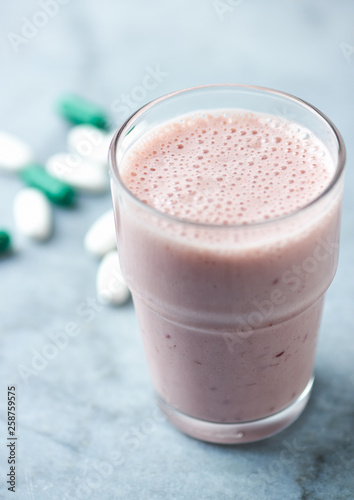 Glass of Protein Shake with milk and raspberries. BCAA amino acids and L - Carnitine capsules in background. Sport nutrition. Bright tone background. Close up. Copy space. 