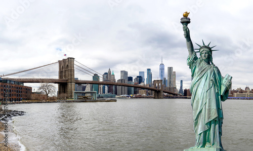 Panorama view of The Statue of Liberty with Brooklyn Bridge and Manhattan downtown sky scraper with cloud blue sky background, Financial district lower Manhattan, New York City, USA.