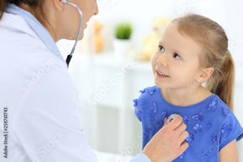 Doctor examining a little girl by stethoscope. Happy smiling child patient at usual medical inspection. Medicine and healthcare concepts