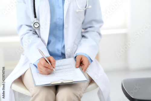 Female doctor writing up medication history records form on clipboard  while sitting at the chair. Physician at work in hospital or clinic. Healthcare  insurance and medicine concept