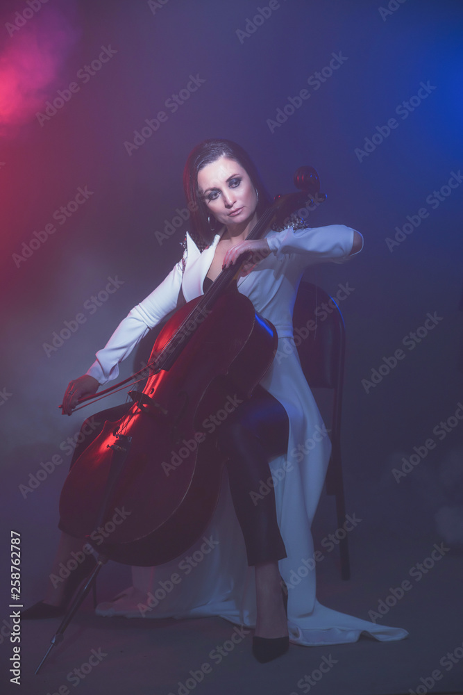 Fototapeta premium Beautiful woman in a white coat plays the cello