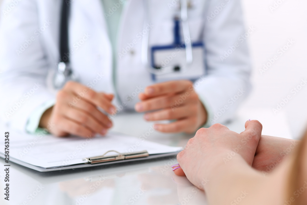 Unknown doctor and patient talking while sitting at the desk in hospital office, close-up of human hands. Medicine and health care concept Unknown doctor and patient talking while sitting at the desk in hospital office, close-up of human hands. Medicine and health care concept