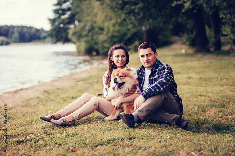 Happy smiling couple resting at the park with a dog.