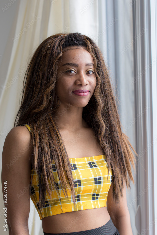 Vertical side lit medium portrait of long-haired mixed race gorgeous thin  smiling young woman standing next to window in cropped top Stock Photo |  Adobe Stock