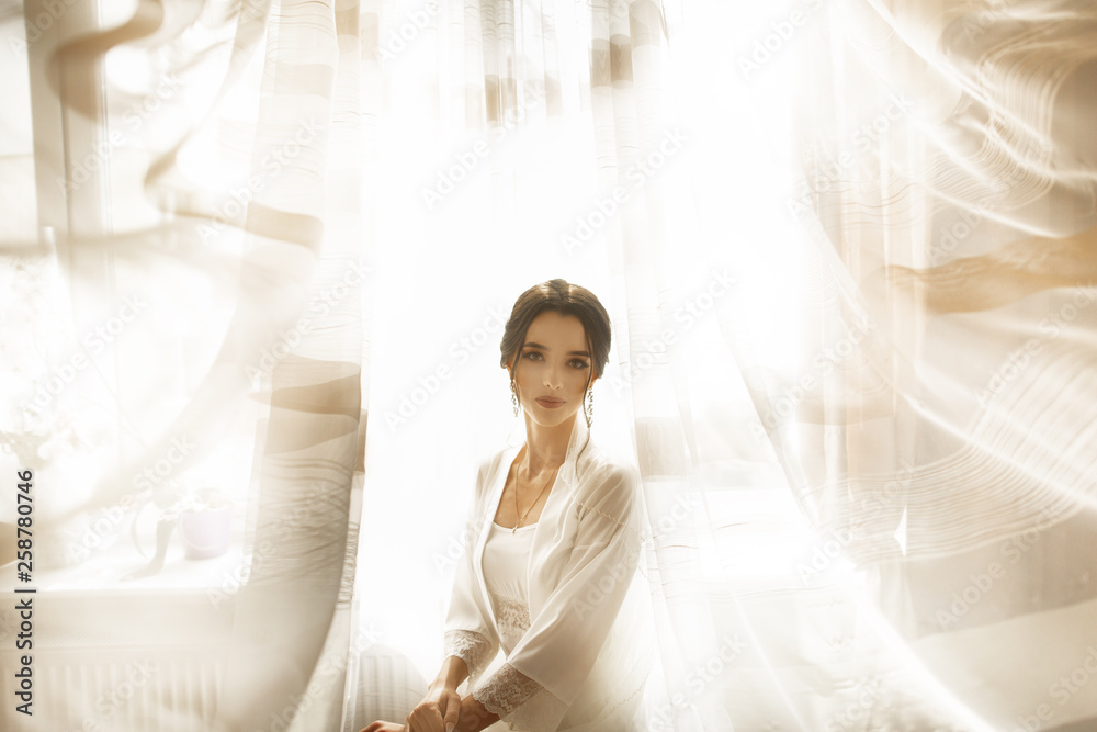 Bride in beautiful dress sitting on chair indoors in white studio interior like at home. Trendy wedding style shot. Bride in beautiful dress sitting on chair indoors in white studio interior like at home. Trendy wedding style shot.