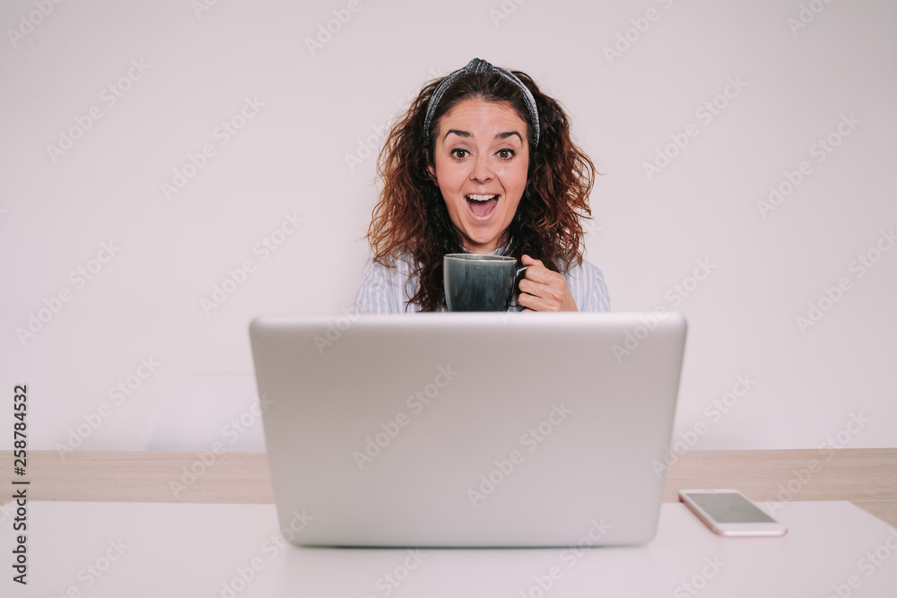 A young woman is surfing the internet while having a cup of coffee. Find something that surprises and makes you very happy. Next to the laptop has a mobile. Everything has a homogenous color. A young woman is surfing the internet while having a cup of coffee. Find something that surprises and makes you very happy. Next to the laptop has a mobile. Everything has a homogenous color.