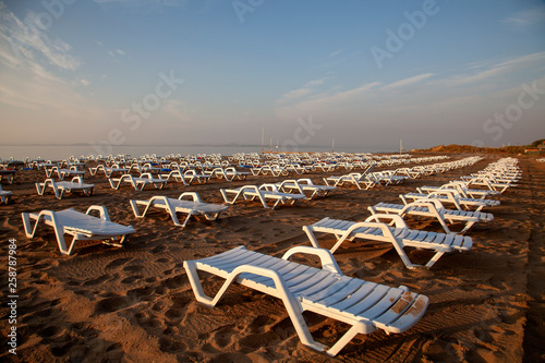 Empty white plastic deck chairs on sandy beach © sayilan