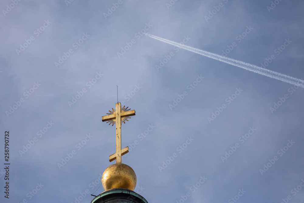 A plane flies high in a cloudless blue sky over a church steeple. fear of superstition