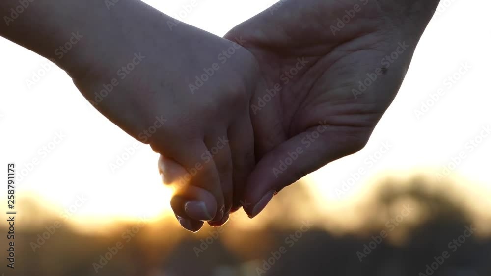 Close the hands of mother and child. Hold hands at sunset. Give a hand to a friend. The sun's rays shine through their fingers. Love, Happiness and Friendship. Hands close up.