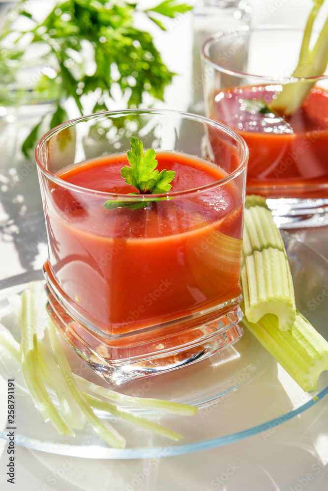 .Tomato juice is poured into a transparent glass with parsley and herring, on a white background, illuminated by sunlight.