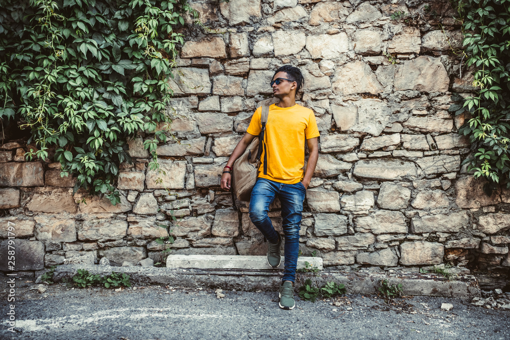 A young Indian man stands near the stone wall. Trendy and fashionable guy.