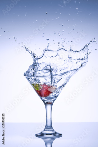 Frozen splashes of clean, spring water, in a glass with frozen strawberries, on a white background.