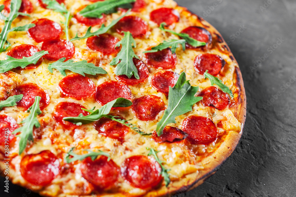 Pepperoni Pizza with Mozzarella cheese, salami, Tomatoes, pepper, Spices and Fresh arugula. Italian pizza on Dark grey black slate background Pepperoni Pizza with Mozzarella cheese, salami, Tomatoes, pepper, Spices and Fresh arugula. Italian pizza on Dark grey black slate background