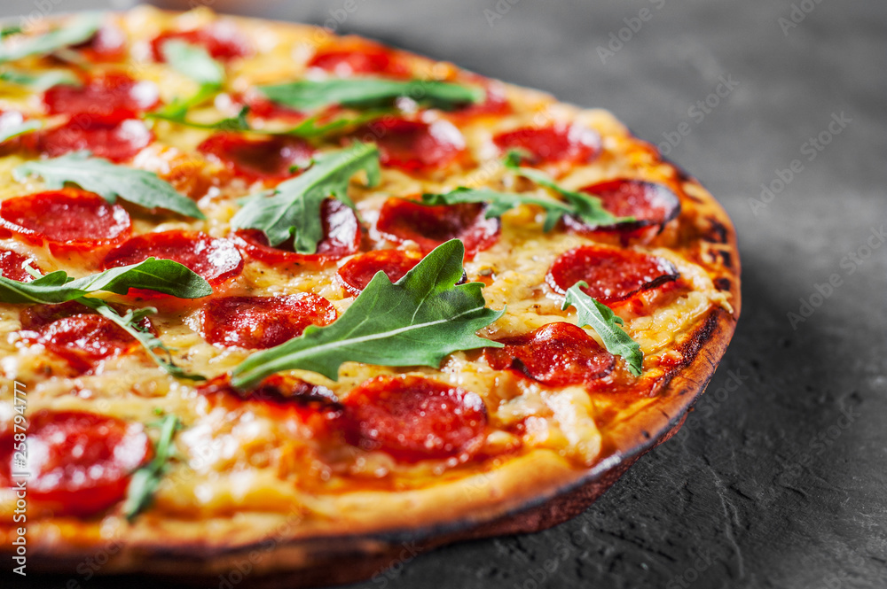Pepperoni Pizza with Mozzarella cheese, salami, Tomatoes, pepper, Spices and Fresh arugula. Italian pizza on Dark grey black slate background