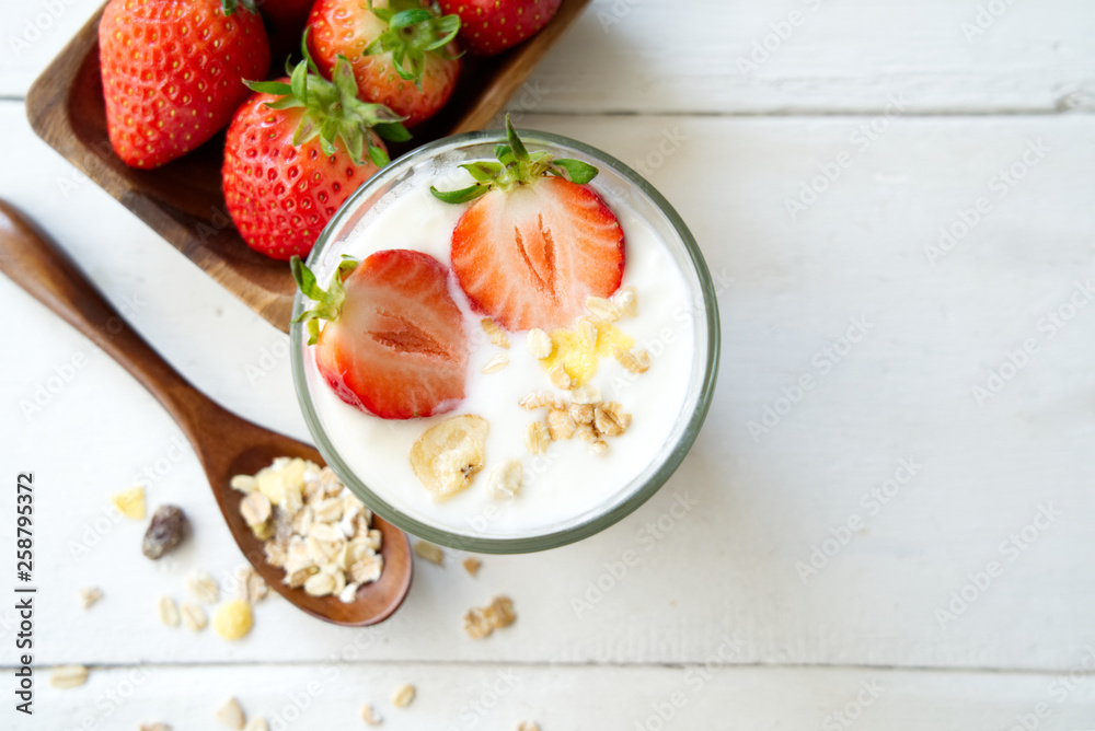 Healthy Greek yogurt with strawberry and muesli in the glass on a old wooden with table decorated with some of muesli and red strawberry and wooden spoon on the table. Seen in top view. Healthy Greek yogurt with strawberry and muesli in the glass on a old wooden with table decorated with some of muesli and red strawberry and wooden spoon on the table. Seen in top view.
