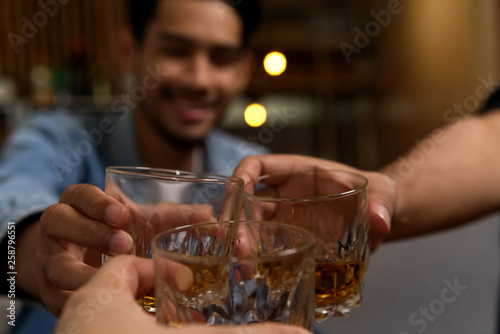 Close up shot of glasses clinking between group of friends drinking whiskey at night party in restaurant. They having so much fun drinking alcohol and talking together. Fun drinking party concept.