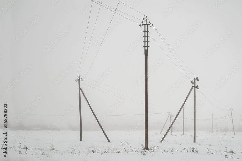 between the wooden supports stretched electrical wires. winter landscape and fog