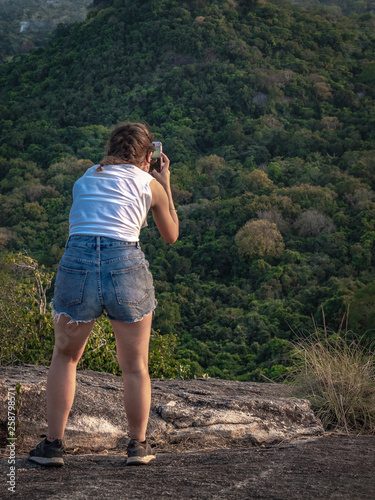 Young caucasian woman taking picture on the top of the Rock Pidurangala. Sri Lanka, March 10, 2019. © Jana Kollarova
