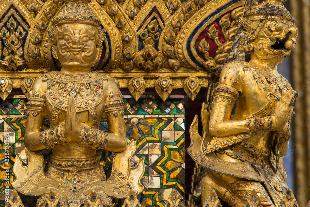 Golden guardian demon statues at the base of a golden Chedi at Bangkok Grand Palace in Thailand