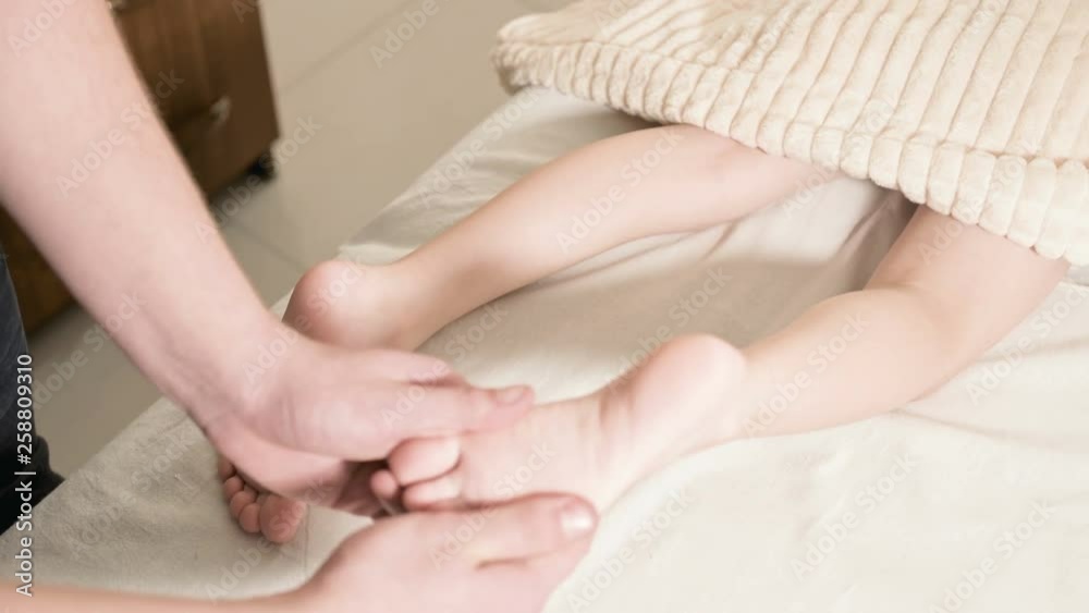 Close-up Male physiotherapist masseur doing a healing relaxing foot massage to a small child lying on a massage bed Close-up Male physiotherapist masseur doing a healing relaxing foot massage to a small child lying on a massage bed