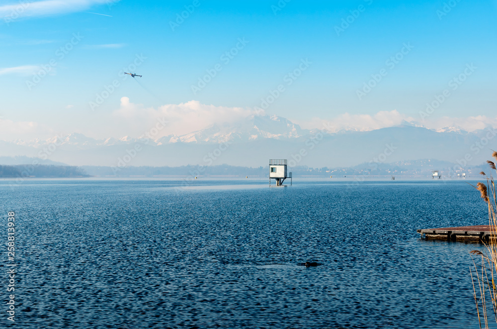 Landscape of Lake Varese on a winter day, with the plane flying over and mountains with snow covered peaks in background.