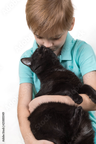 Caucasian boy embraces gently the black adult cat. The cat answers with mutual love, caresses and reaches the muzzle for the face of the boy