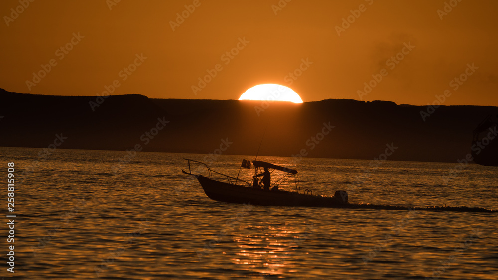 A boat slips between the water and the sun on its way back to port in La Paz Mexico.