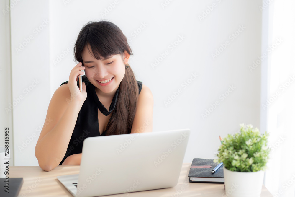 Beautiful young freelance asian woman smiling working on laptop computer and talking mobile smart phone at desk office with professional, girl using notebook, business and lifestyle concept. Beautiful young freelance asian woman smiling working on laptop computer and talking mobile smart phone at desk office with professional, girl using notebook, business and lifestyle concept.