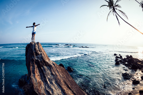 Successful woman outstretched arms on seaside rock cliff edge