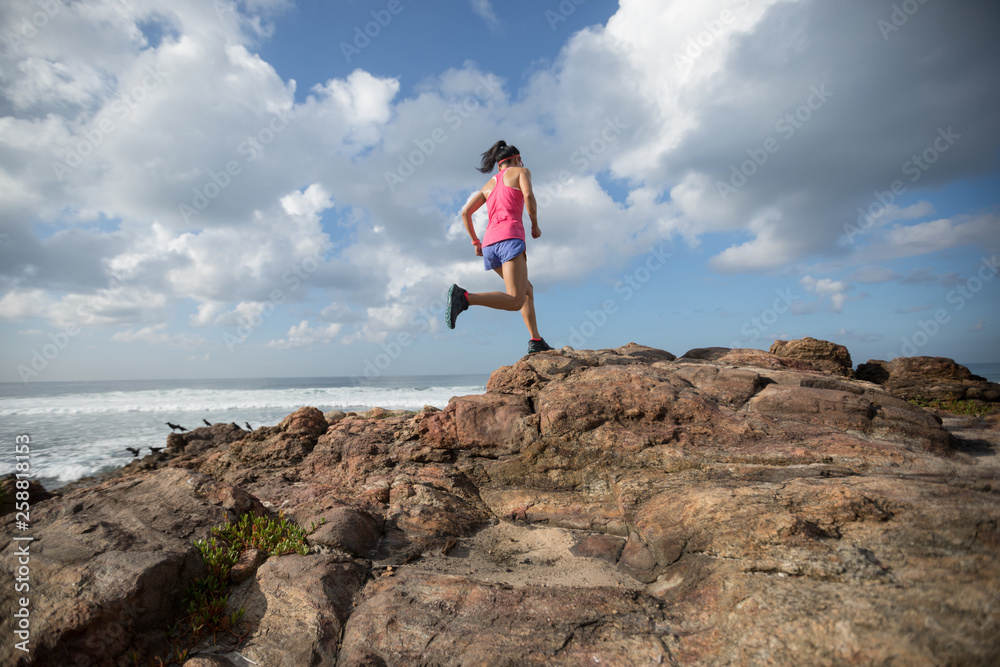 Young fitness woman trail runner running to rocky mountain top on seaside Young fitness woman trail runner running to rocky mountain top on seaside