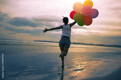 young asian woman running and jumping on seaside with colored balloons