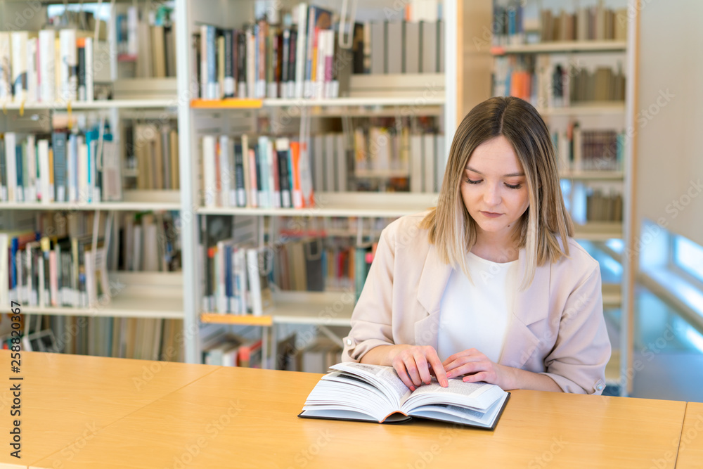 Young beautiful caucasian girl reading a book in the library pointing with her finger Young beautiful caucasian girl reading a book in the library pointing with her finger