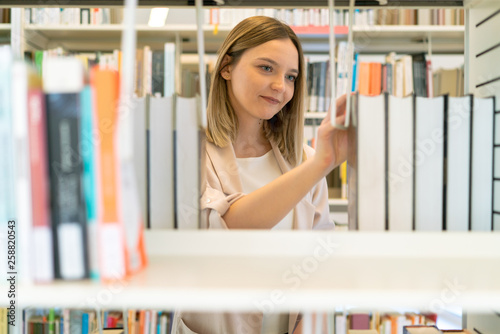 Young beautiful caucasian girl happy choosing books on the bookshelf in the library