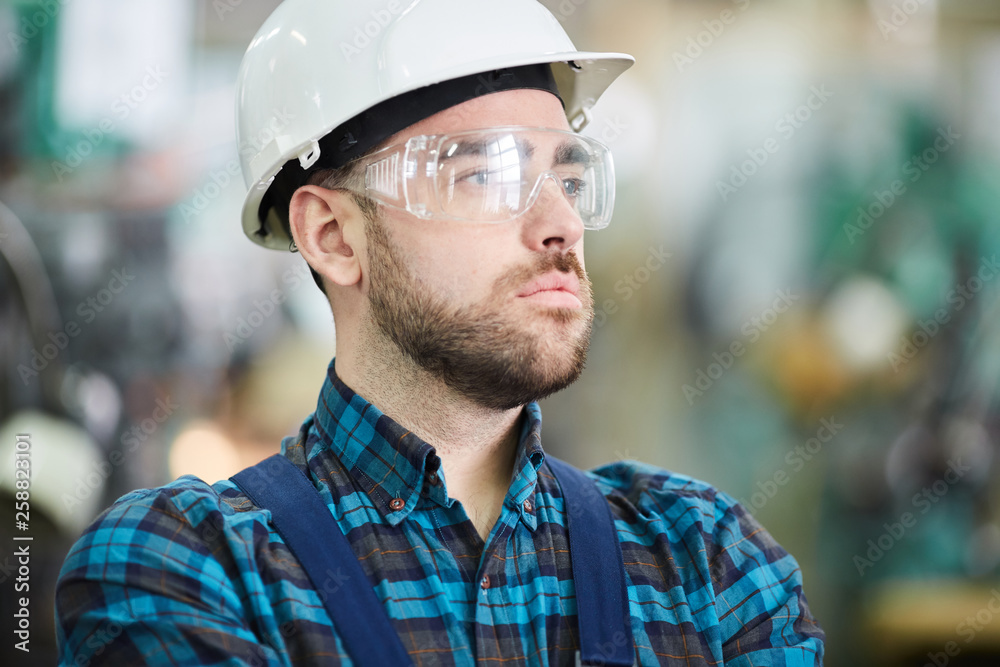Head and shoulders portrit of bearded factory worker wearing hardhat looking away pensively, copy space Head and shoulders portrit of bearded factory worker wearing hardhat looking away pensively, copy space