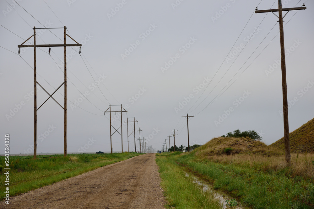 Empty road, rows of utility poles and high voltage power lines, rural Texas