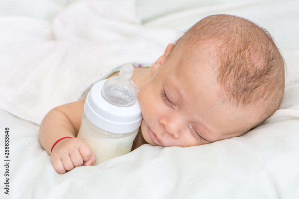 newborn baby curled up sleeping on a blanket with feeding bottle newborn baby curled up sleeping on a blanket with feeding bottle