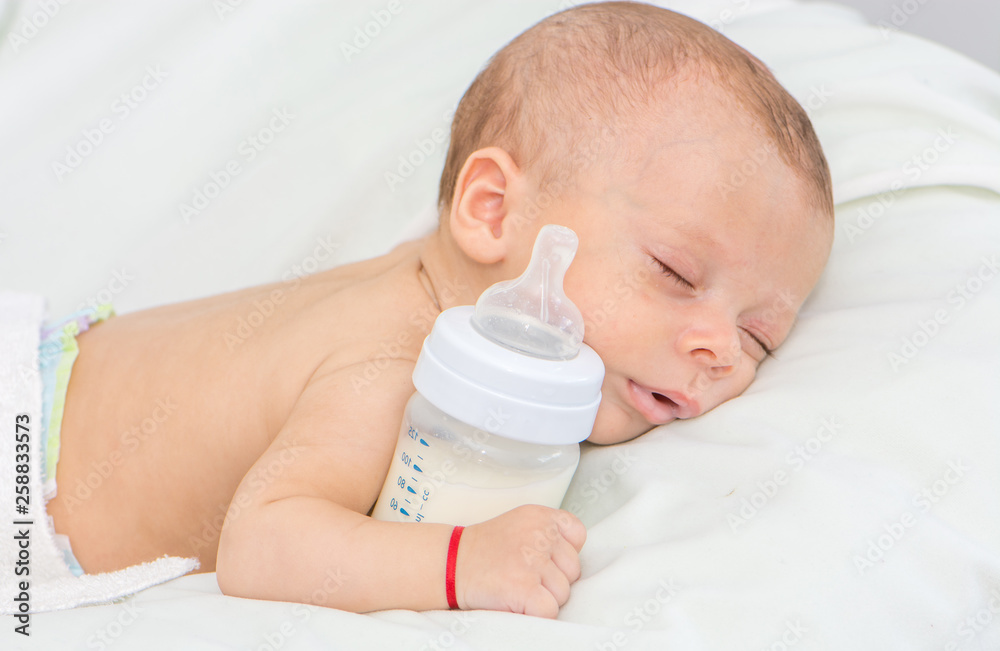 newborn baby curled up sleeping on a blanket with feeding bottle newborn baby curled up sleeping on a blanket with feeding bottle
