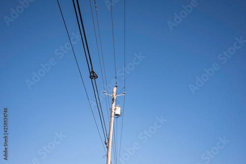 Electric poles with wires and cables set on a bright blue daylight sky.