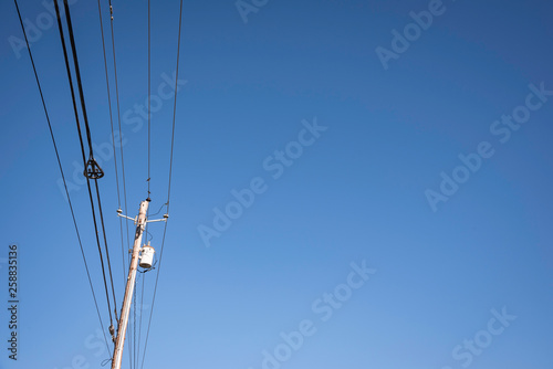 Electric poles with wires and cables set on a bright blue daylight sky.