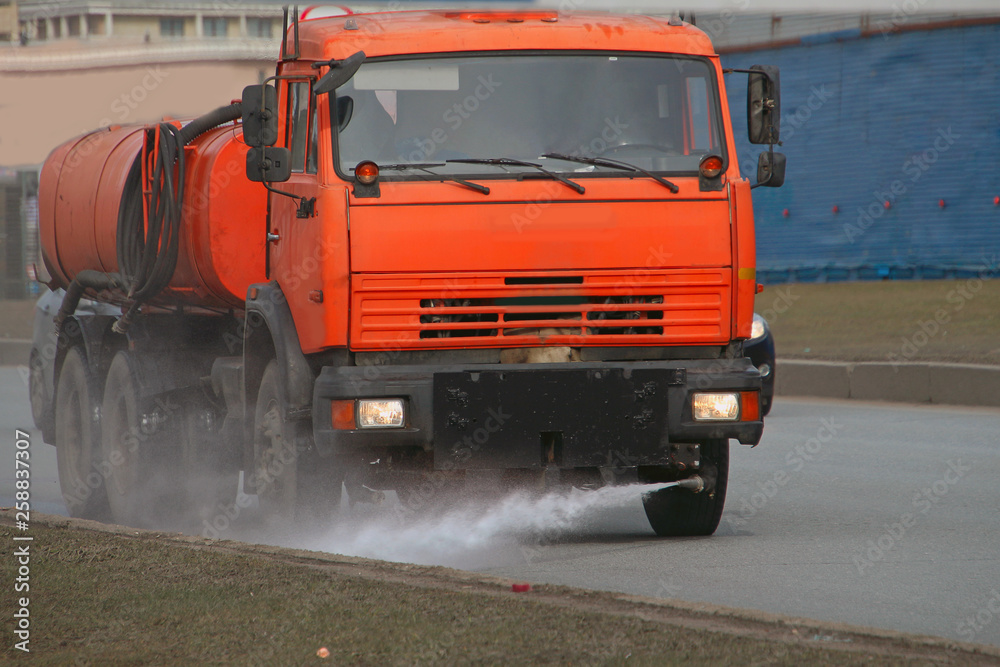 big orange watering machine washes the road part with water   