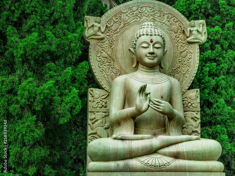 Buddha statue be smile made from wooden with green tree backdrop on the temple, Thailand.