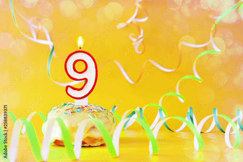 Nine years birthday. Cupcake with burning candle in the form of number 9. Bright yellow background with copy space