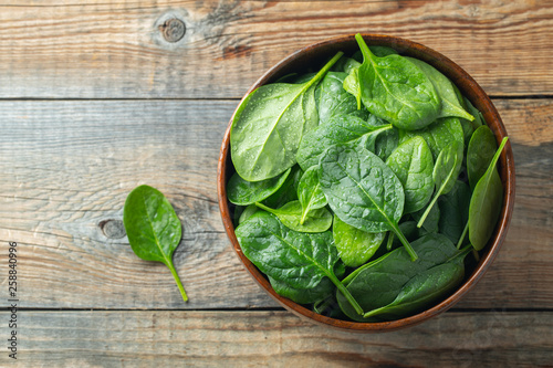 Fresh spinach leaves in bowl on wooden table.